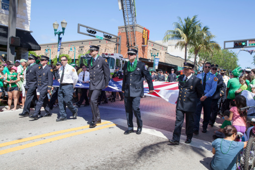 Delray Beach, United States - March 17, 2013: Uniformed marchers at the St. Patrick's Day parade come down the street.  Onlookers watch from the sidewalk.  The St. Patrick’s Day Parade is an annual event in Delray Beach that began in 1968 when an Irish local pub owner took a walk down Delray's main street with his Shillelagh and a green pig and declared it “my own parade.” Now Uniformed Emergency Service workers as well as commercial, civic, charitable, educational, and social groups participate. Groups throughout the United States and several foreign countries take part. Saint Patrick is the patron saint of Ireland. A good time is always had by adults and children alike at Delray’s parade in tribute to St. Patrick.