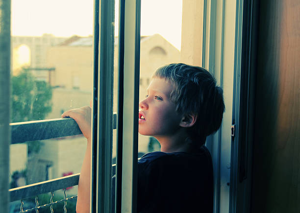 istock Cute 7 years old boy looks out the window 475817906