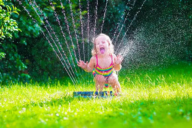 Photo of Little girl playing with garden water sprinkler