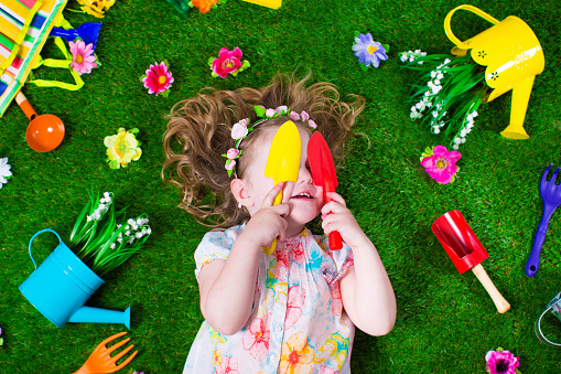 Kids gardening. Children with garden tools. Child with watering can and shovel. Little kid watering flowers. Girl relaxing on green backyard lawn in summer.