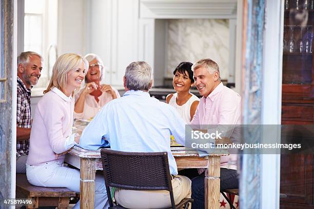 Group Of Mature Friends Enjoying Meal At Home Together Stock Photo - Download Image Now