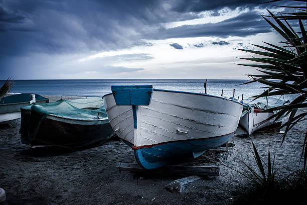 EN - Boat in the foreground with other boats nearby, on the beach at sunset. Typical image of the Ligurian landscape and of Italian seafood countries.