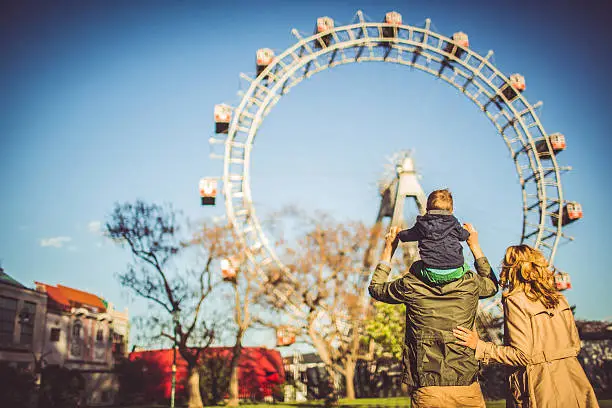 Young family walking through the amusement park, after numerous of fun carousel rides. Shot from behind.