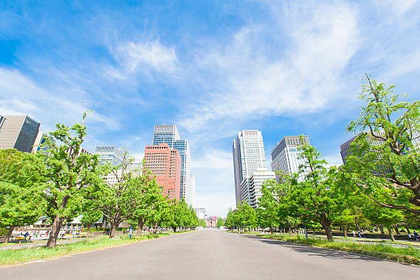 Tokyo, Japan - April 1, 2018: Park with people walking on sidewalk by Imperial palace during spring day with cityscape skyscrapers in downtown and construction crane