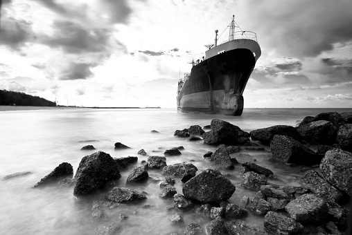 Cargo ship run aground on rocky  shore waiting for rescue.