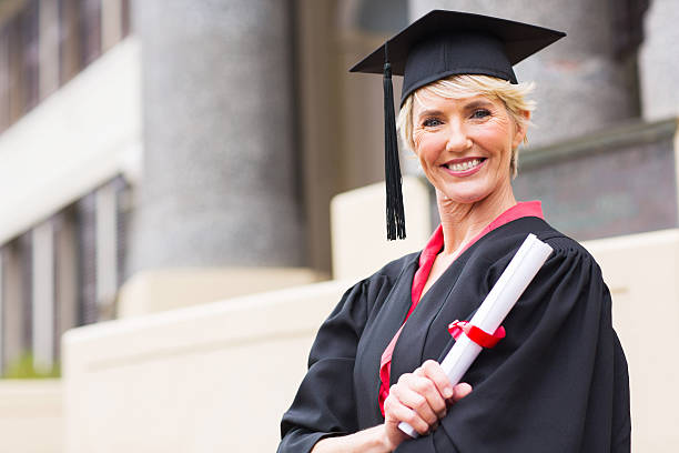 istock middle aged woman with graduation cap and gown 475846717