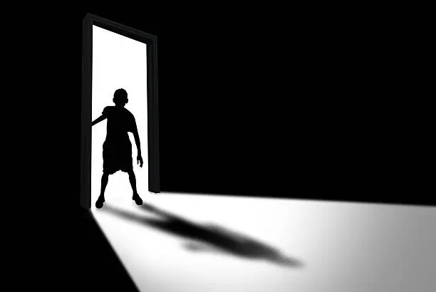 Silhouette of boy entering dark room with bright light in doorway