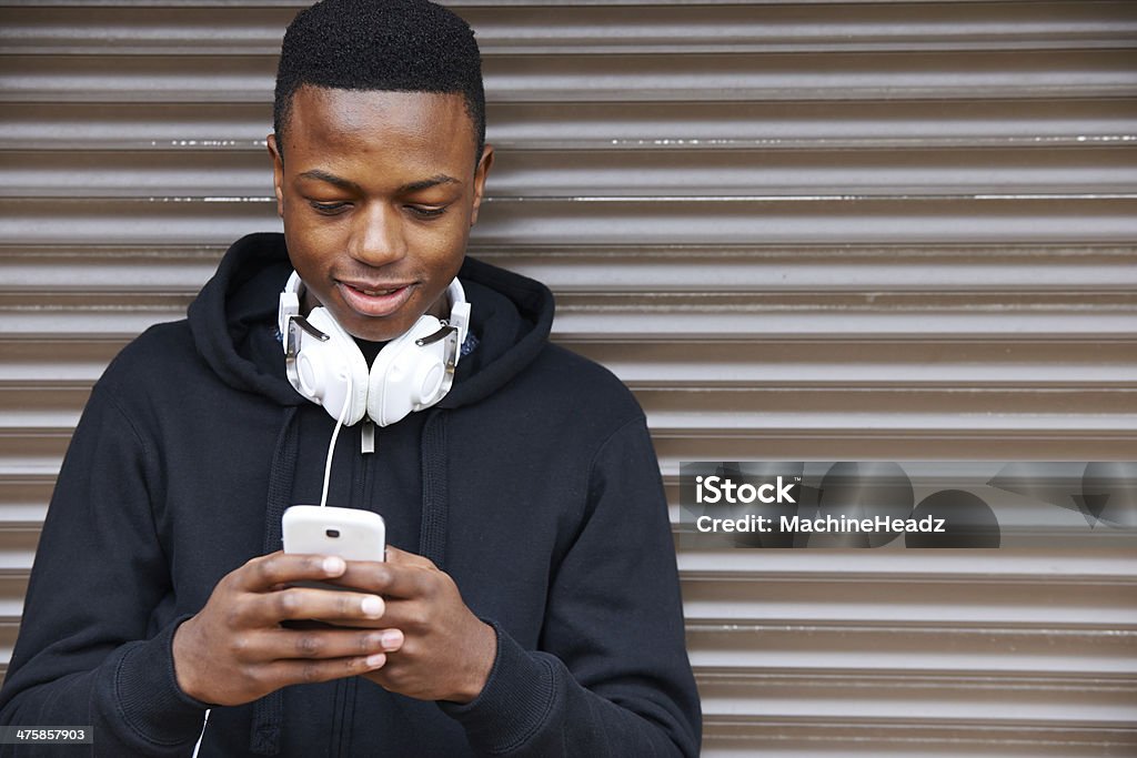Teenage Boy Listening To Music And Using Phone Pleased to be living in a buzzing city Teenager Stock Photo