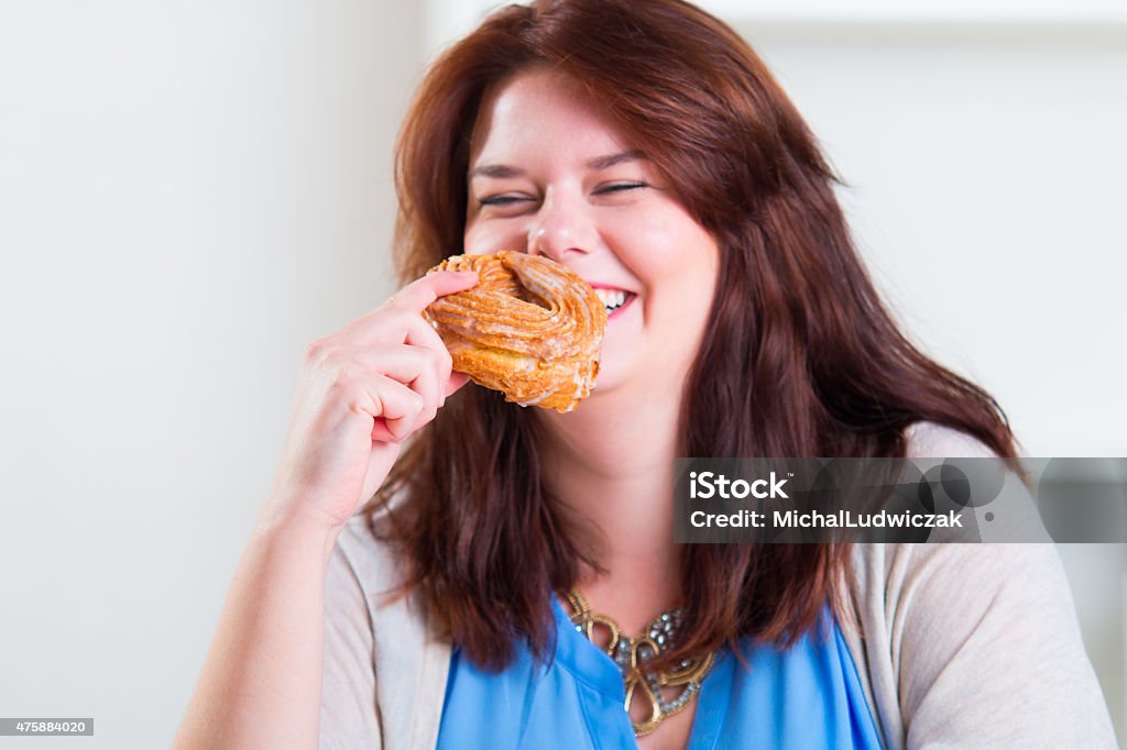 Plump and happy woman eating donuts at the table Plump and cheerful woman eating donuts at the table 2015 Stock Photo