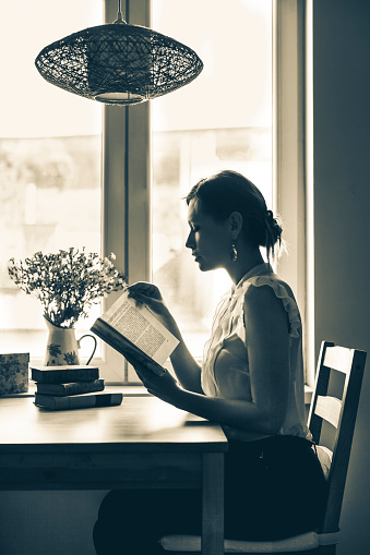 Silhouette of a woman that is reading at home. Candid shot. Low key portrait.