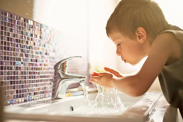 Little boy drinking tap water. Little boy aged 4 is drinking tap water in sunlit bathroom.