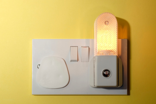 A child's nursery bedroom nightlight plugged in to wall socket with a safety cap fitted to the other unused socket