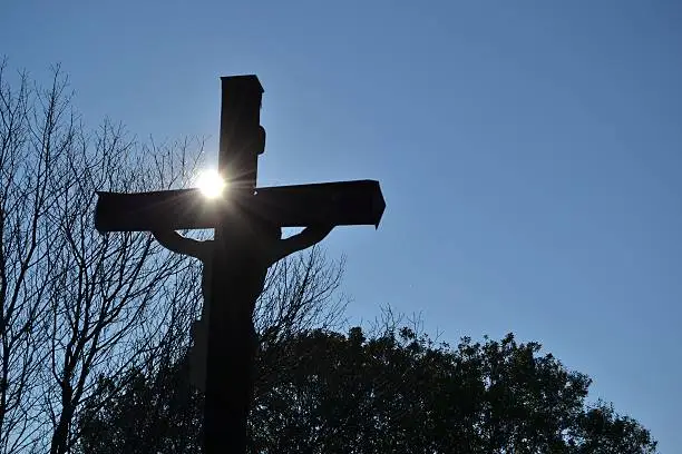 Sun behind the crucifix in the landscape, relaxation and religious photo, suitable for announcements