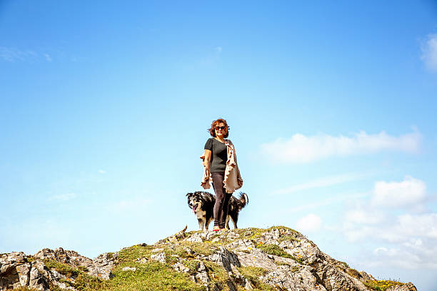 Mature hispanic woman standing on remote coastal headland with border collie