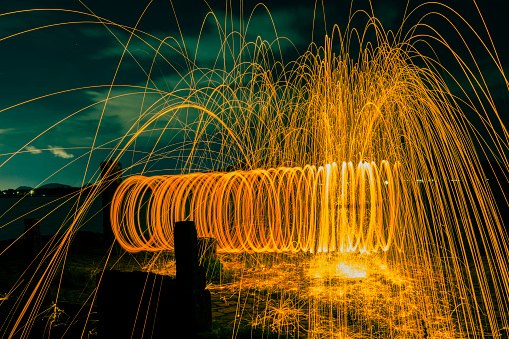 Firework showers of hot glowing sparks from spinning steel wool on the beach.