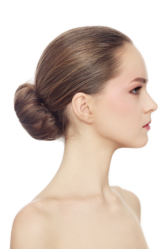 Profile portrait of young beautiful girl with hair bun over white background