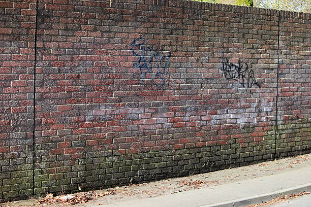 istock Image of dirty red-brick wall, spray-painted graffiti tags, run-down area 475920538