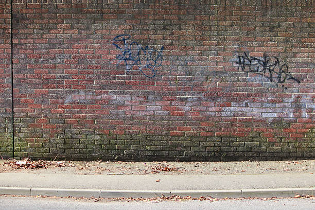 istock Image of red brick wall, graffiti writing tags, tarmac pavement 475920544