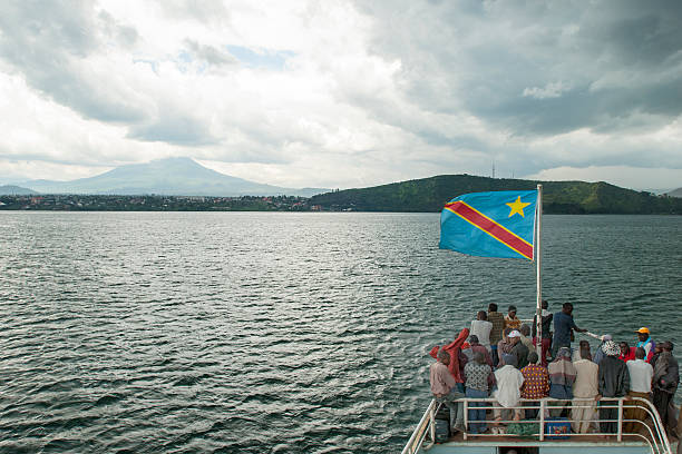 Congolese boat on Lake Kivu is approaching Goma Lake Kivu, Democratic Republic of Congo - October 26, 2007: A boat with African people is travelling under the flag of the Democratic Republic of Congo at Lake Kivu. The boat is approaching the town of Goma, the capital of the province of North Kivu in DR Congo. In the background the 3470 m high Mt. Nyiragongo Volcano is visible.  lake kivu stock pictures, royalty-free photos & images