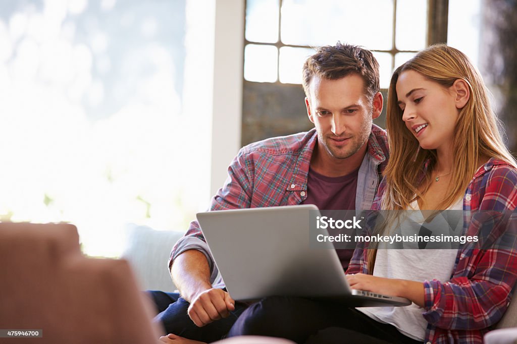 Couple At Home In Lounge Using Laptop Computer Couple - Relationship Stock Photo