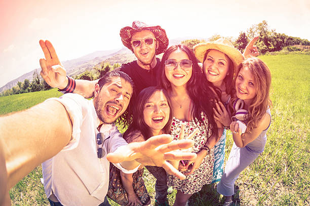 Happy best friends using selfie stick at countryside picnic