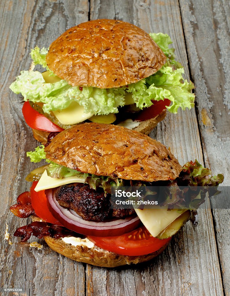 Hamburgers Tasty Homemade Hamburgers with Roasted Beef, Lettuce,Tomato, Onions, Cheese, Bacon and Pickle on Whole Wheat Bun closeup on Rustic Wooden background 2015 Stock Photo