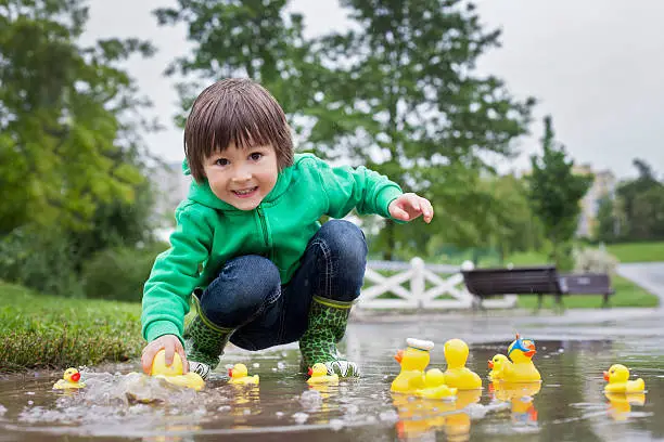 Photo of Little boy, jumping in muddy puddles in the park