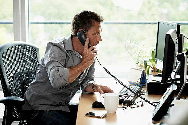 Business man working in modern office Businessman looking at computer while on the phone in a modern office rolled up sleeves stock pictures, royalty-free photos & images