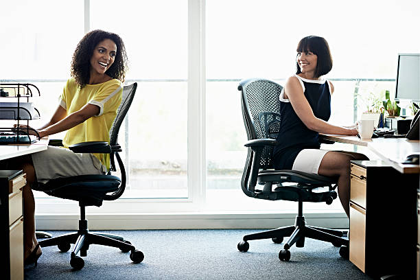 female coworkers laughing - bürostuhl stock-fotos und bilder