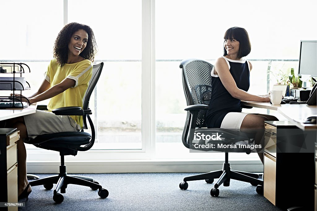 Female coworkers laughing Two female coworkers laughing in a modern office Office Chair Stock Photo