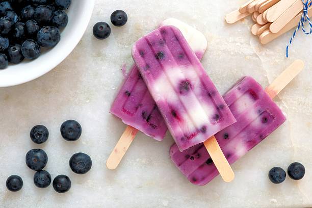 Blueberry vanilla popsicles on a white marble background Blueberry vanilla popsicles in a cluster with fresh berries on a white marble background flavored ice photos stock pictures, royalty-free photos & images