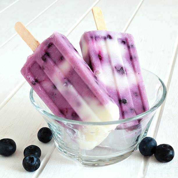 istock Blueberry vanilla popsicles in a clear bowl against white wood 475970228