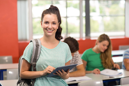 Portrait of happy female student using digital tablet in classroom
