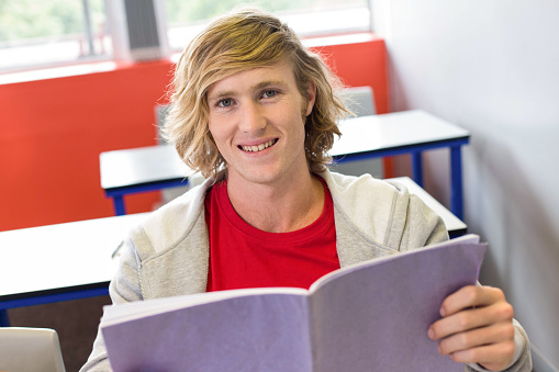Portrait of smiling male student reading notes in classroom