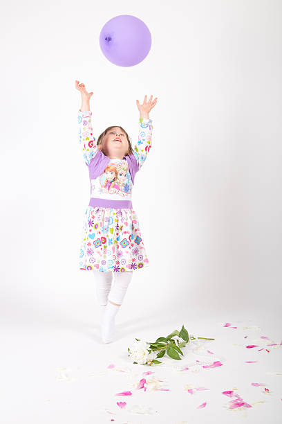 3.5 years old young child, playing purple balloon. Studio shot. She wears purple clothes, roses ad petals on the floor.