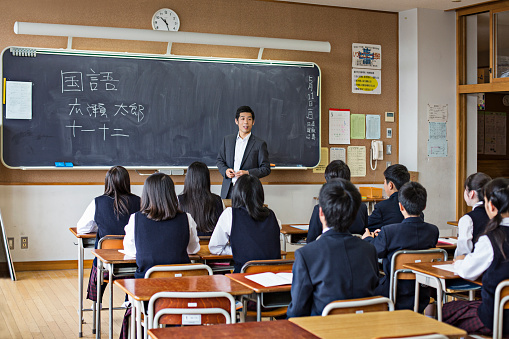 Japanese children listening to their teacher on a class, kids are wearing the school uniform.