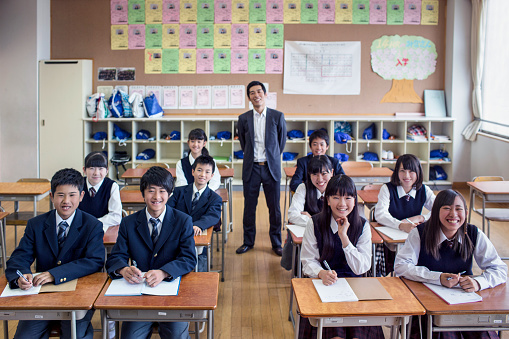 Japanese classroom with children and teacher in the background looking at the camera.