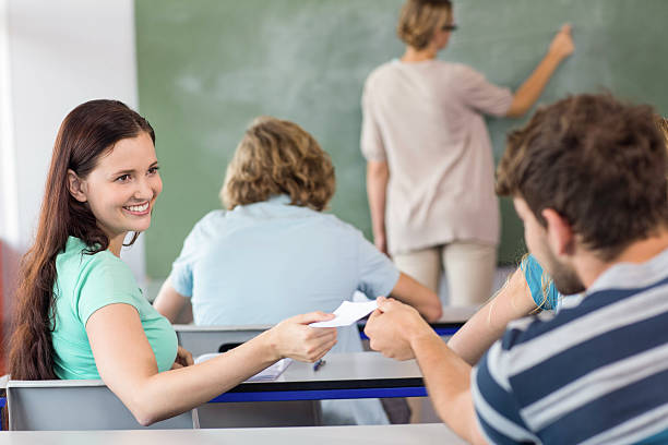 istock Female student passing note to friend in classroom 475991138