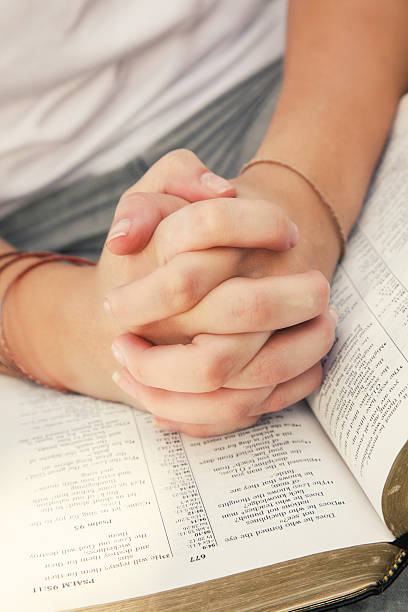 istock Young woman's hands folded in prayer on top of Bible 475991604