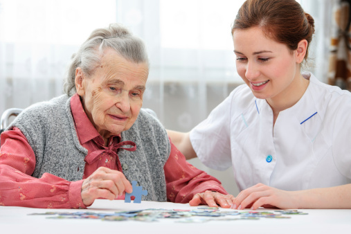 Nurse helps the senior woman jigsaw puzzle to solve in a nursing home