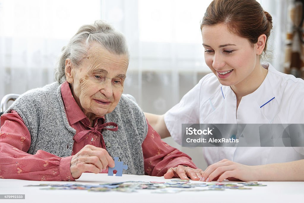 Senior woman with her caregiver Nurse helps the senior woman jigsaw puzzle to solve in a nursing home Senior Adult Stock Photo