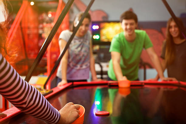 Four friends having fun and playing air hockey game Four friends having fun and playing air hockey game arcade photos stock pictures, royalty-free photos & images