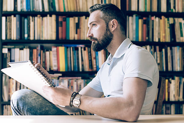 istock young bearded creative man sketching in front of bookshelf 475995938