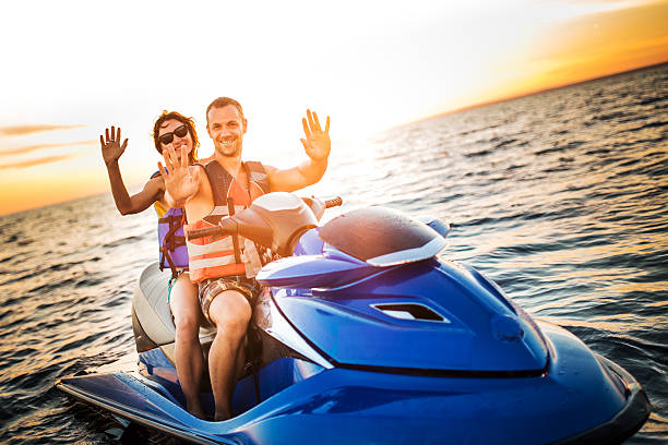 Couple Riding  Jet Boat Couple looking at camera while riding a water scooter on the sea at the sunset, lens flare. jet boat stock pictures, royalty-free photos & images