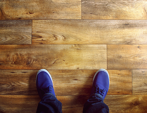 Man's feet with blue snickers on the wooden floor. Background
