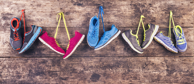 Five pairs of various running shoes hang on a nail on a wooden fence background