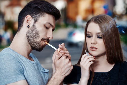 man lighiting up cigarettea and girl smoking from one, cool teenager in urban scene.