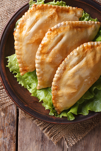 Traditional pies empanadas on a plate with lettuce close-up. vertical view above, rustic style