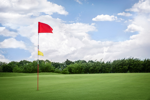 Red golf flag on green fairway with beautiful blue sky, with empty copyspace.