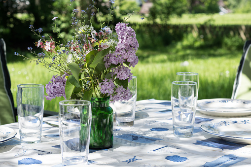 rural decorated garden table with dishes, glasses and flowers to eat outside in the early summer